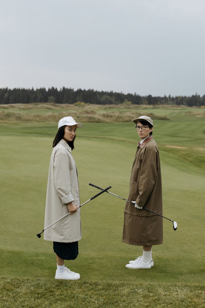 A fashionable couple posing with golf clubs on a scenic golf course.